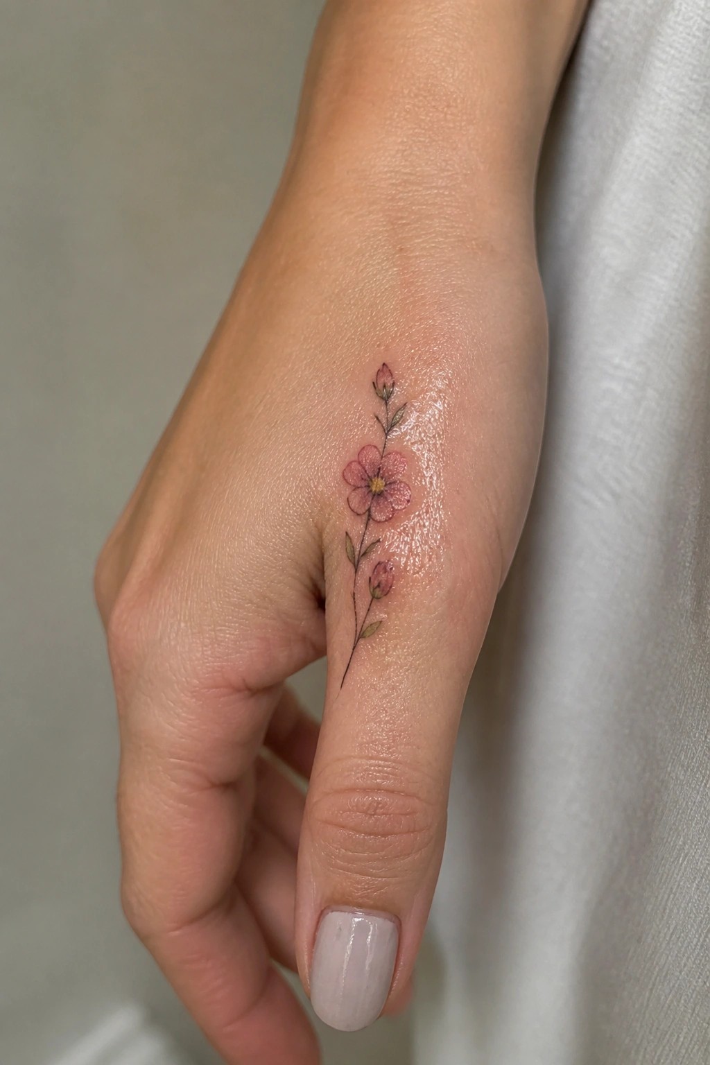 Delicate pink flower tattoo with stem and buds on a hand
