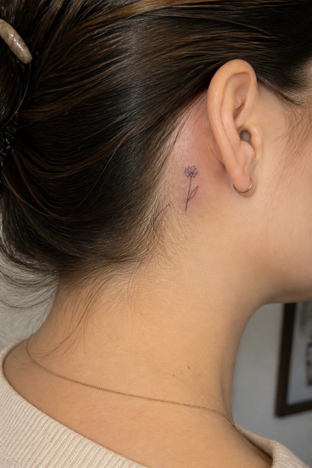 Tiny purple flower tattoo behind ear on neck with gold earring and necklace