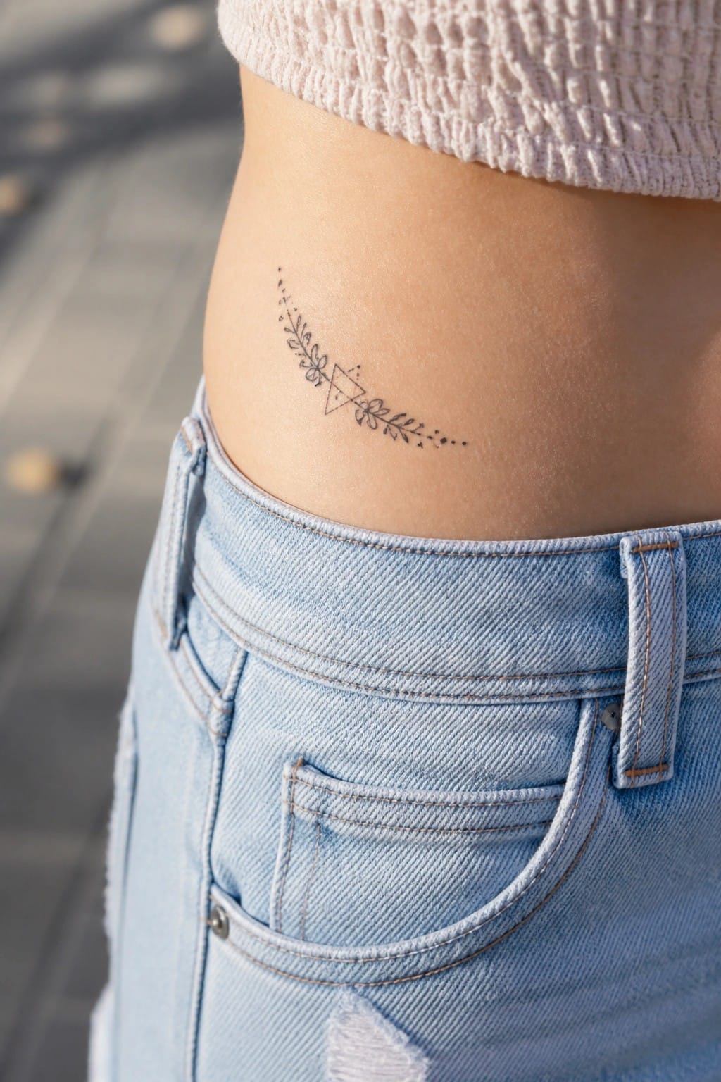 Geometric floral tattoo on hip above light blue denim jeans and pink knit top