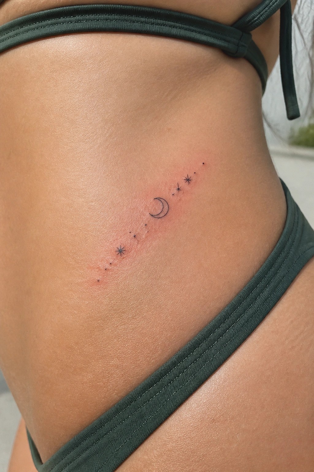 Fresh crescent moon and stars tattoo on reddened skin beside green bikini