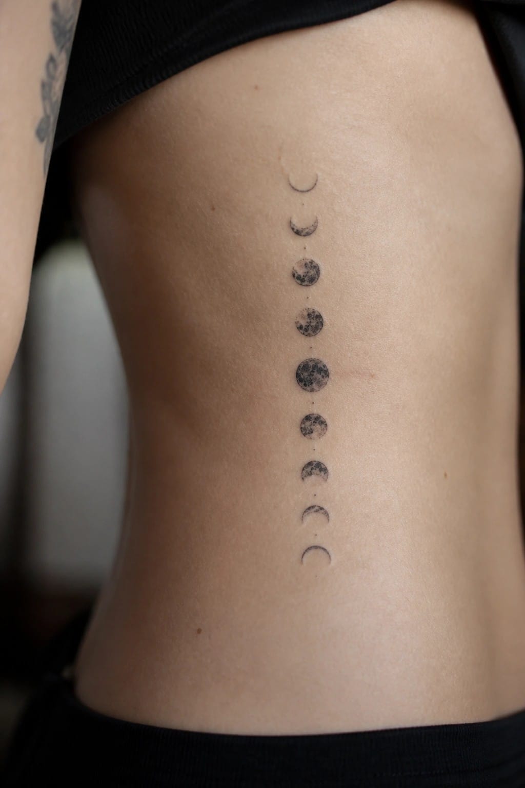 Vertical moon phase tattoo running down a person's back in black top