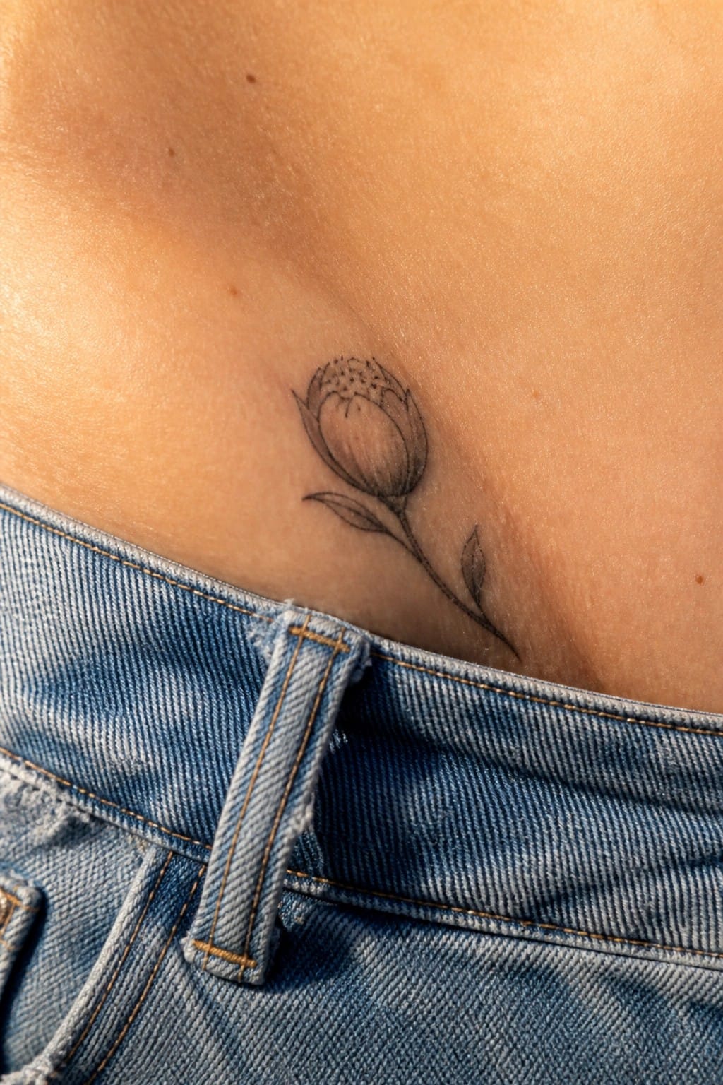 Black floral tattoo on skin above blue denim jeans waistband