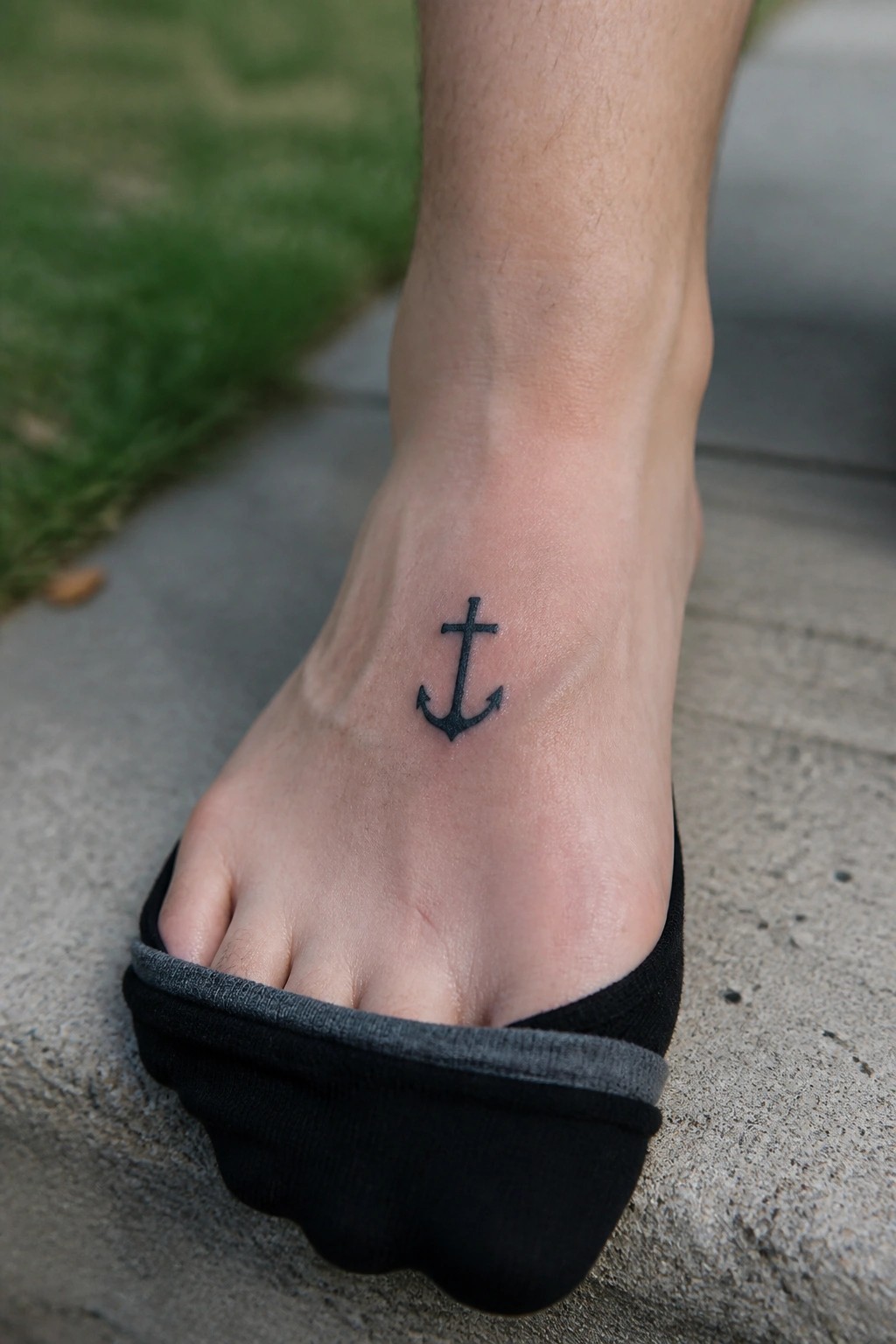 Black anchor tattoo on foot with black sock pulled down on pavement