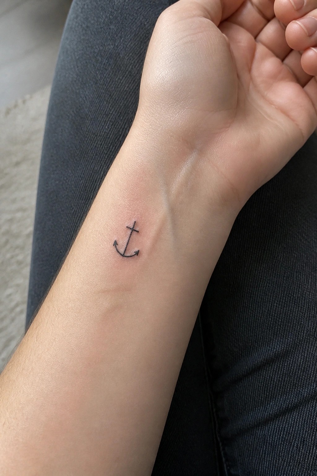 Small black anchor tattoo on light-skinned wrist against dark clothing.