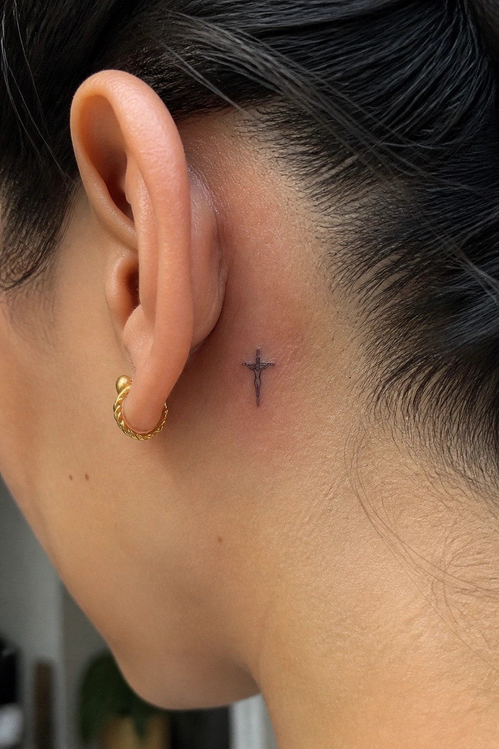 Small black crucifix tattoo with a figure of Jesus placed behind the ear on the side of the head