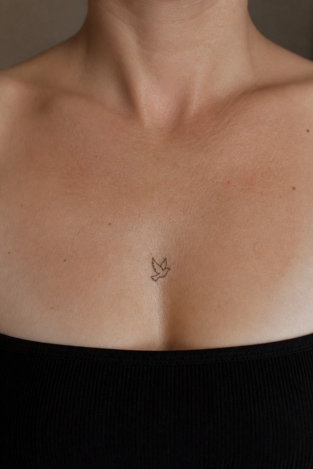 Small bird tattoo centered on freckled chest above black top