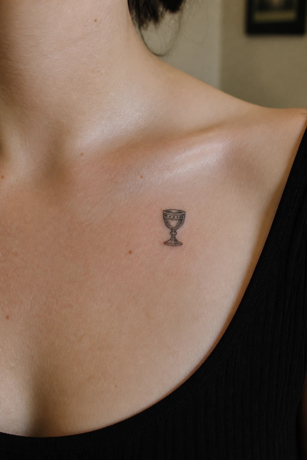 Small ornate goblet tattoo on collarbone above black top on light skin