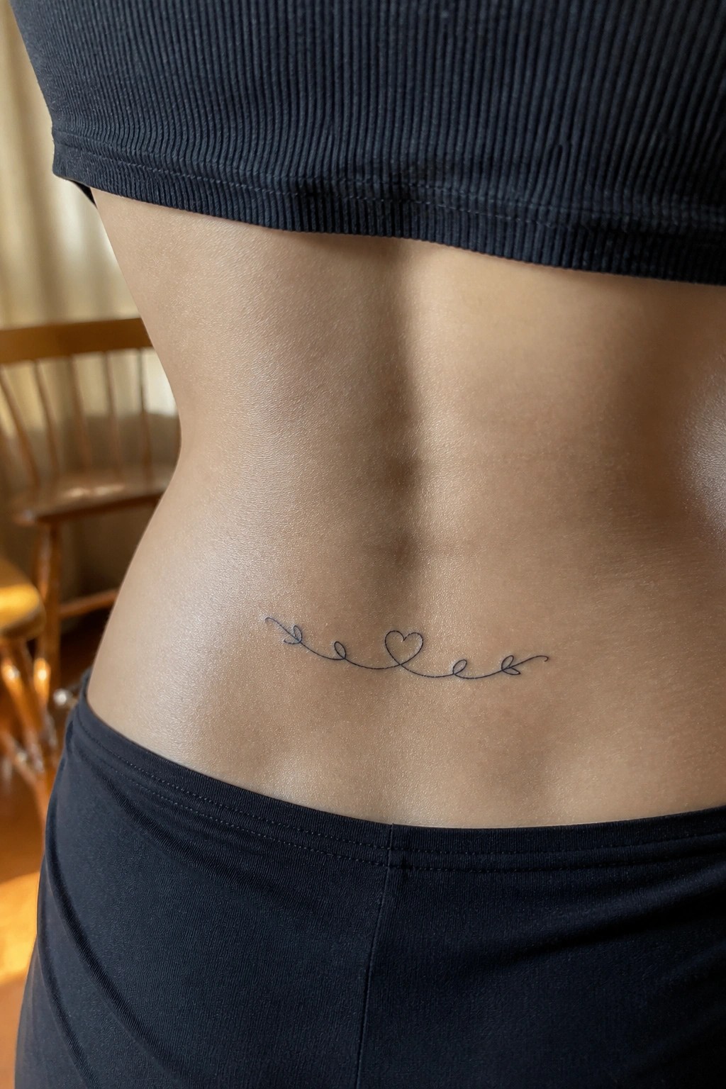 Minimalist line tattoo with heart on lower back below black crop top