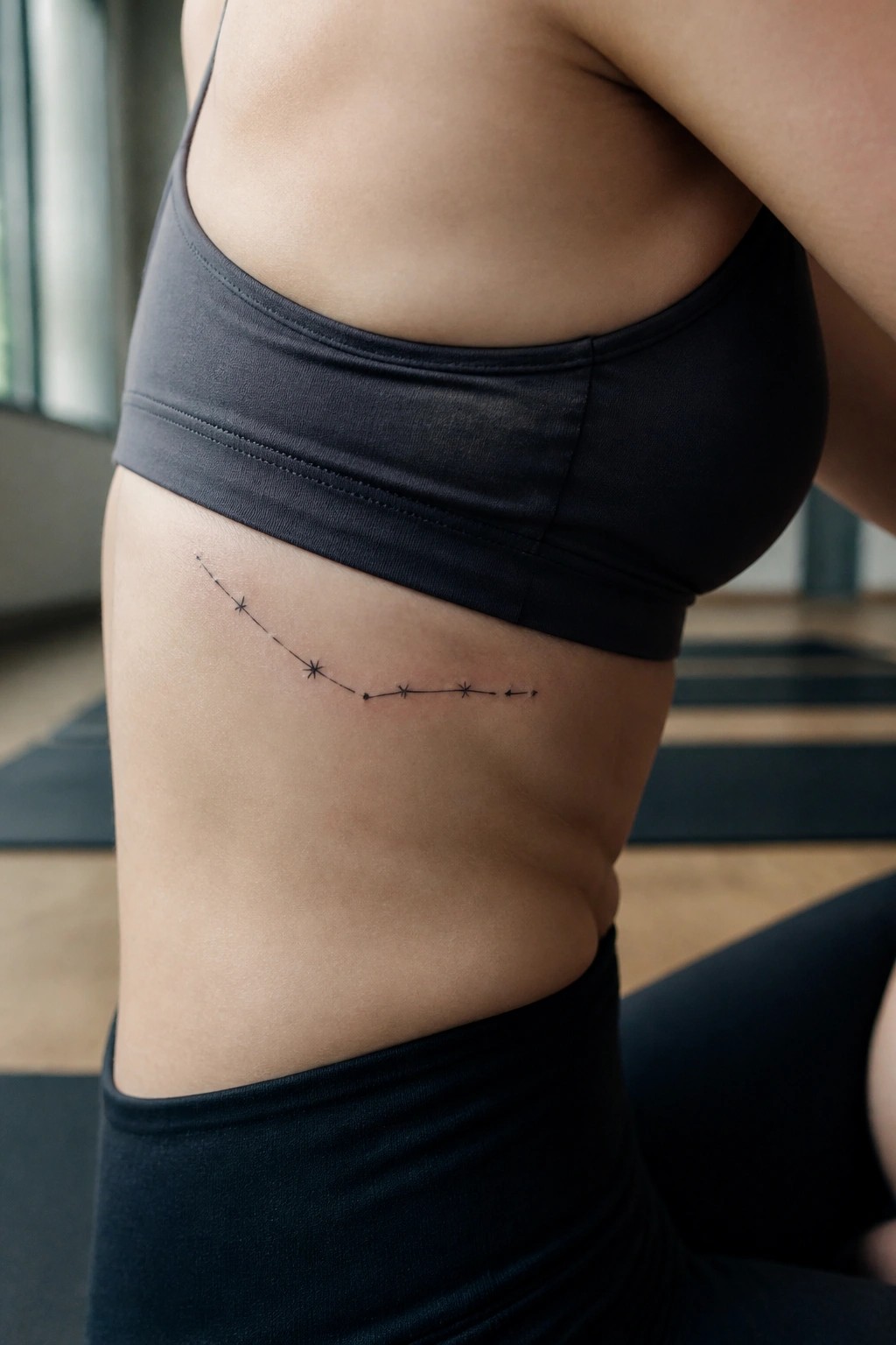 Woman's torso in gray sports bra with constellation tattoo on ribs.