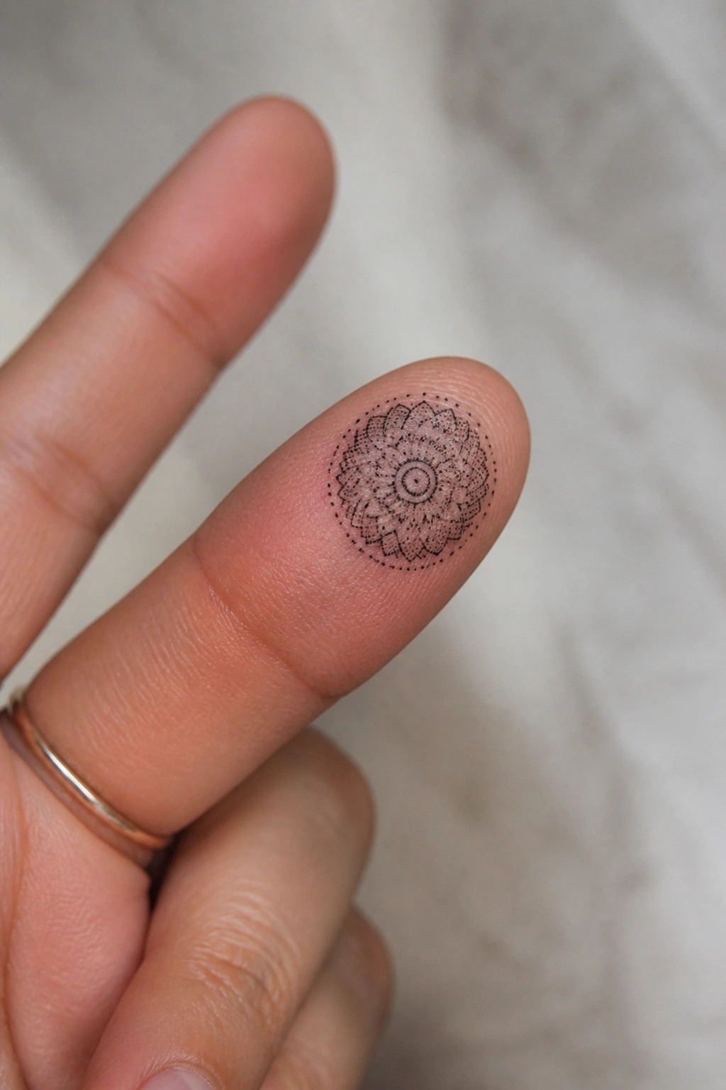 Intricate black mandala tattoo on fingertip beside thin gold ring on hand.