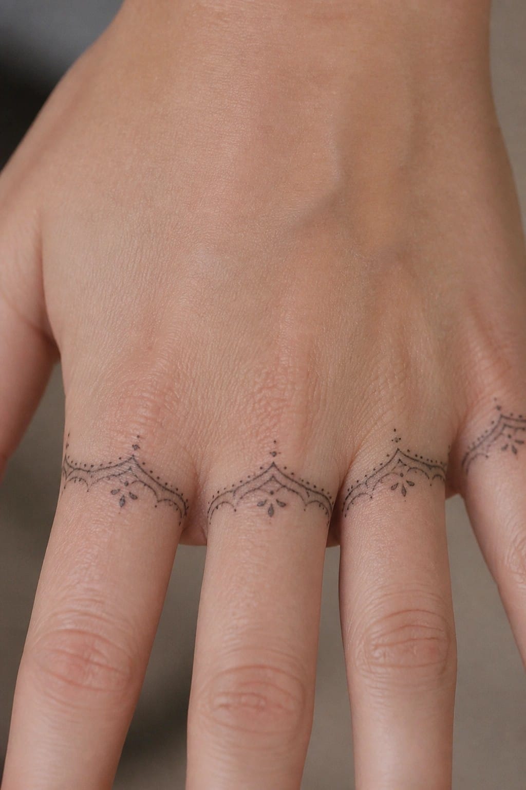 Close up of fine line arched tattoos with dots on the bases of four fingers