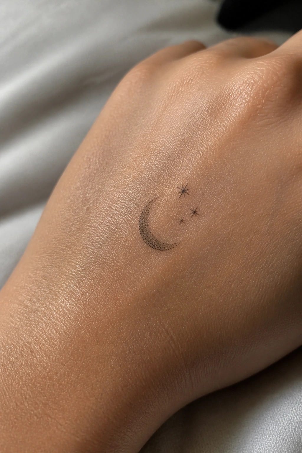 Small crescent moon and three stars tattoo on the back of a hand using fine dotwork lines.