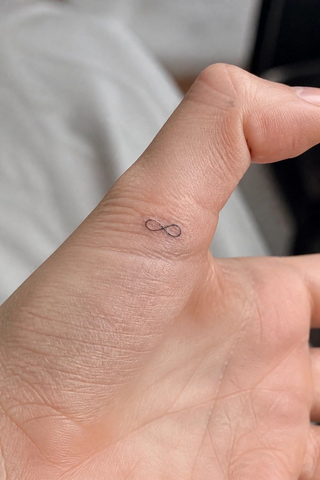 Small black infinity symbol tattoo on the side of a finger near the knuckle