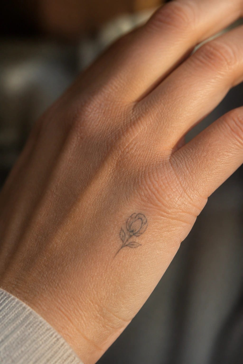 Close-up of a hand with a small rose tattoo and light sweater cuff.