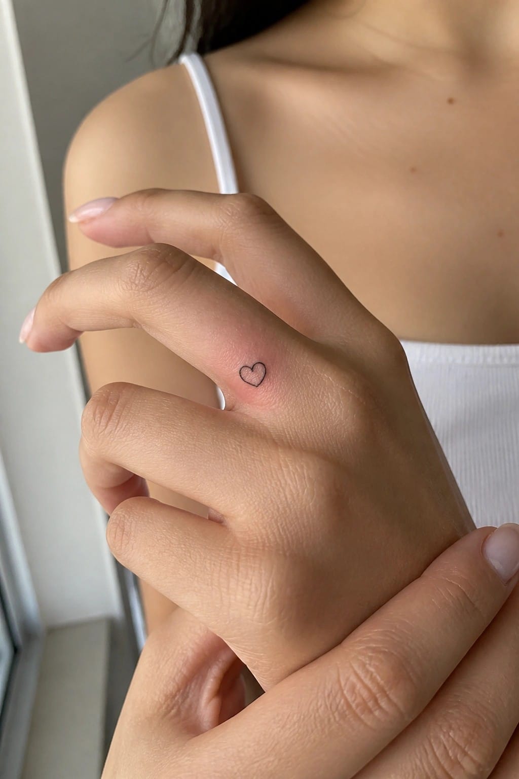 Hand with small heart tattoo on ring finger held by another with manicured nails