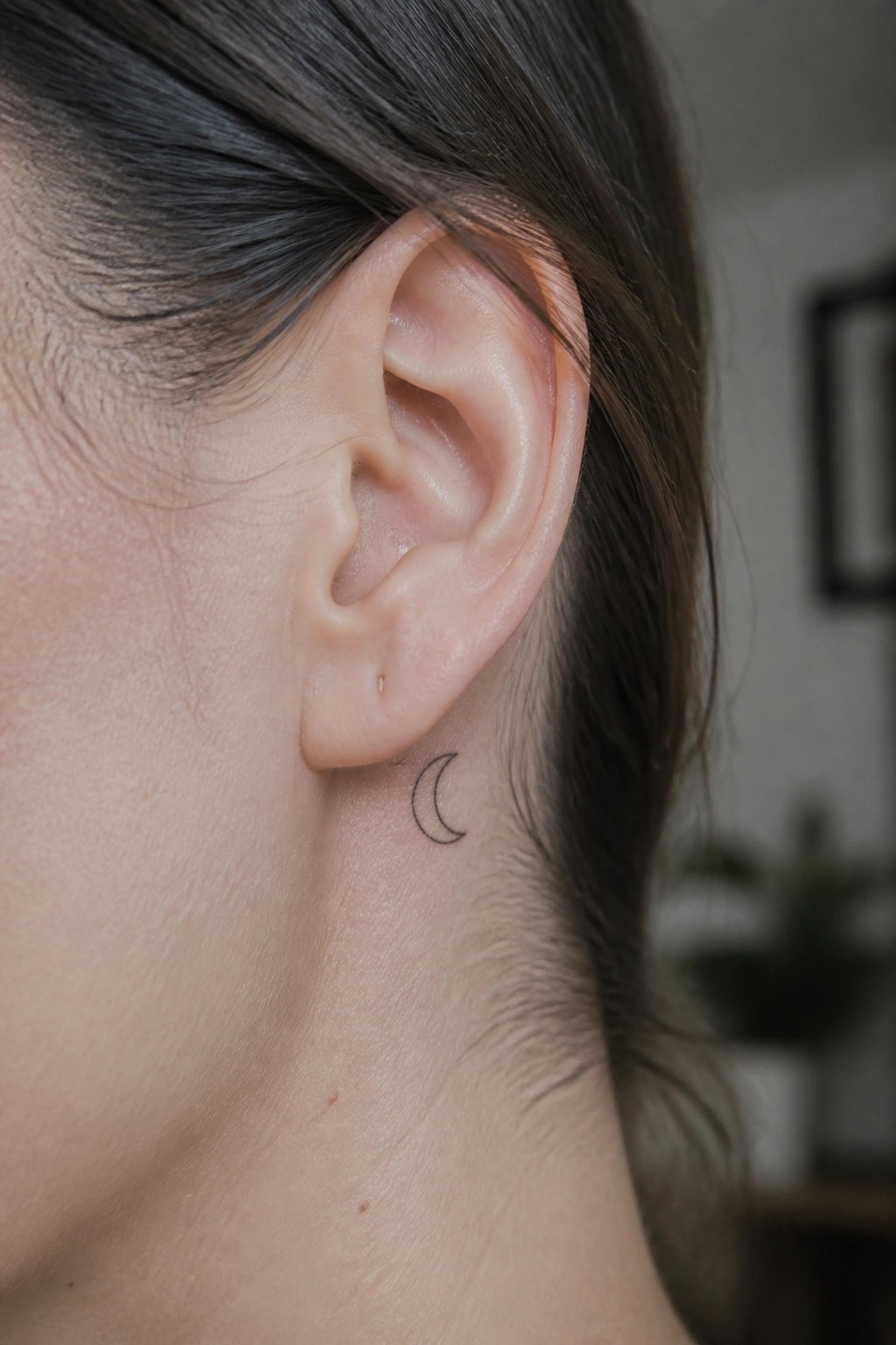Close-up of an ear with crescent moon tattoo and small gold stud earrings.