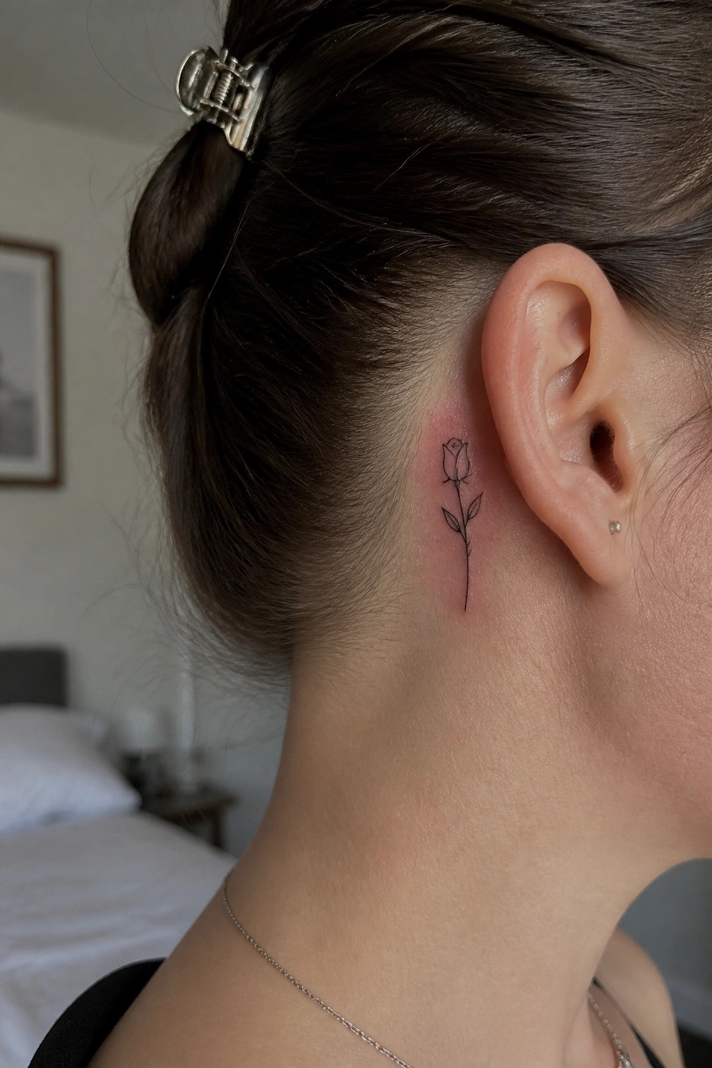 Woman with dark bun and silver clip shows rose tattoo behind ear