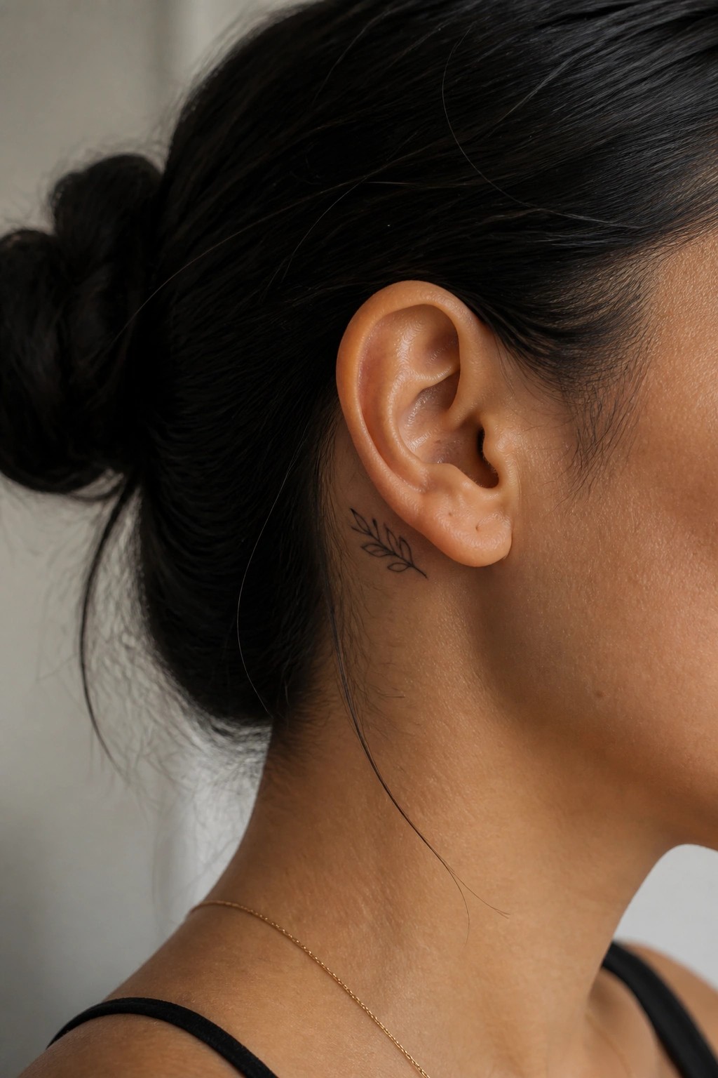 Woman's neck and ear with leaf tattoo, dark bun, thin gold necklace