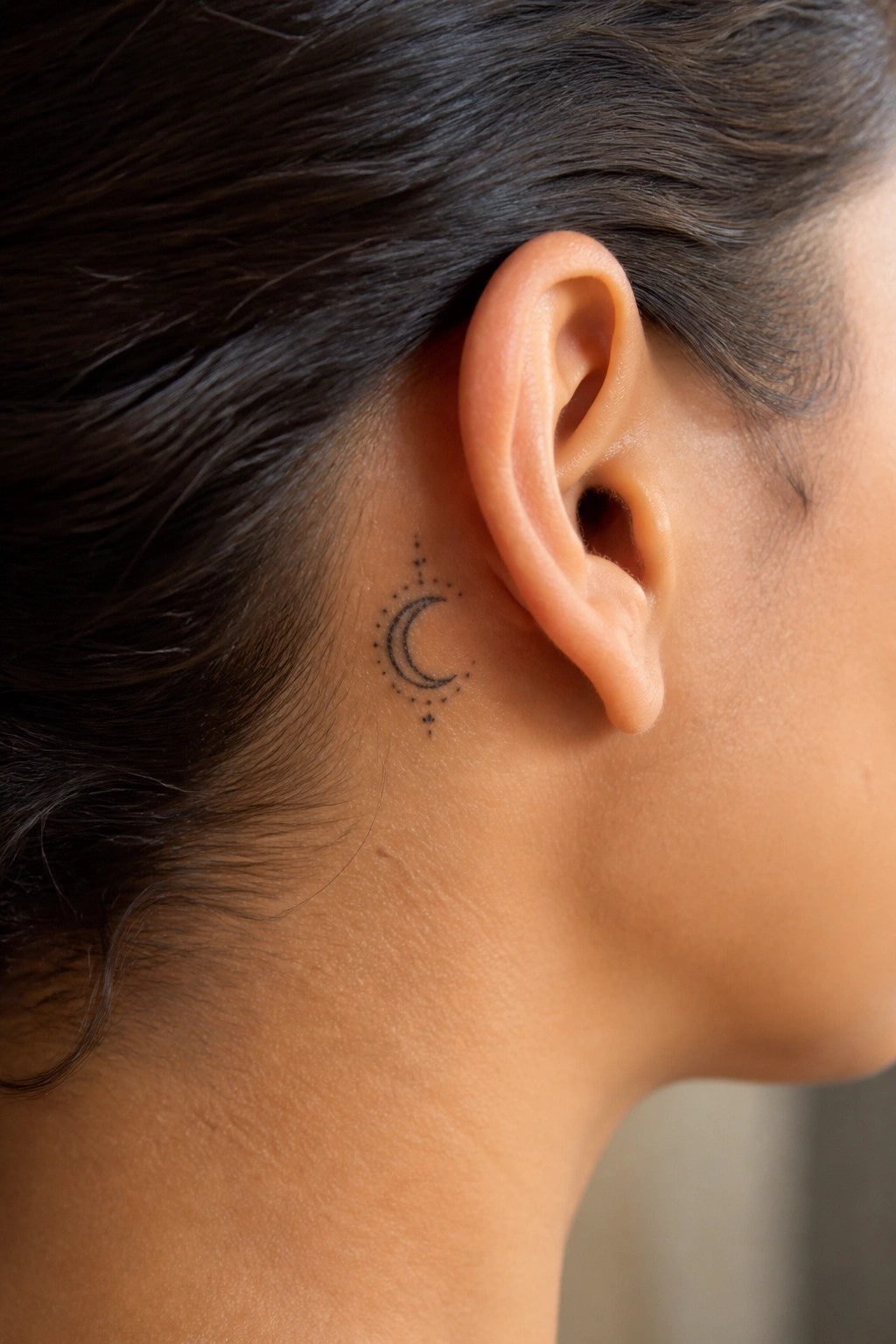 Crescent moon tattoo with stars behind a person's ear and dark hair