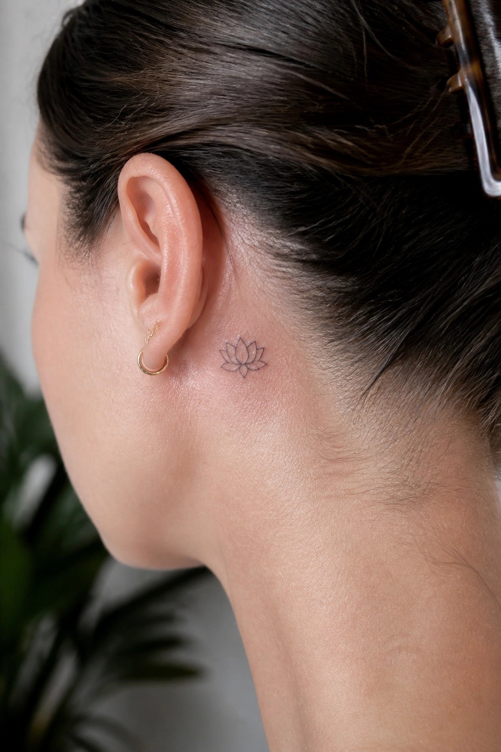 Close-up of ear with gold hoop earring and lotus tattoo behind it