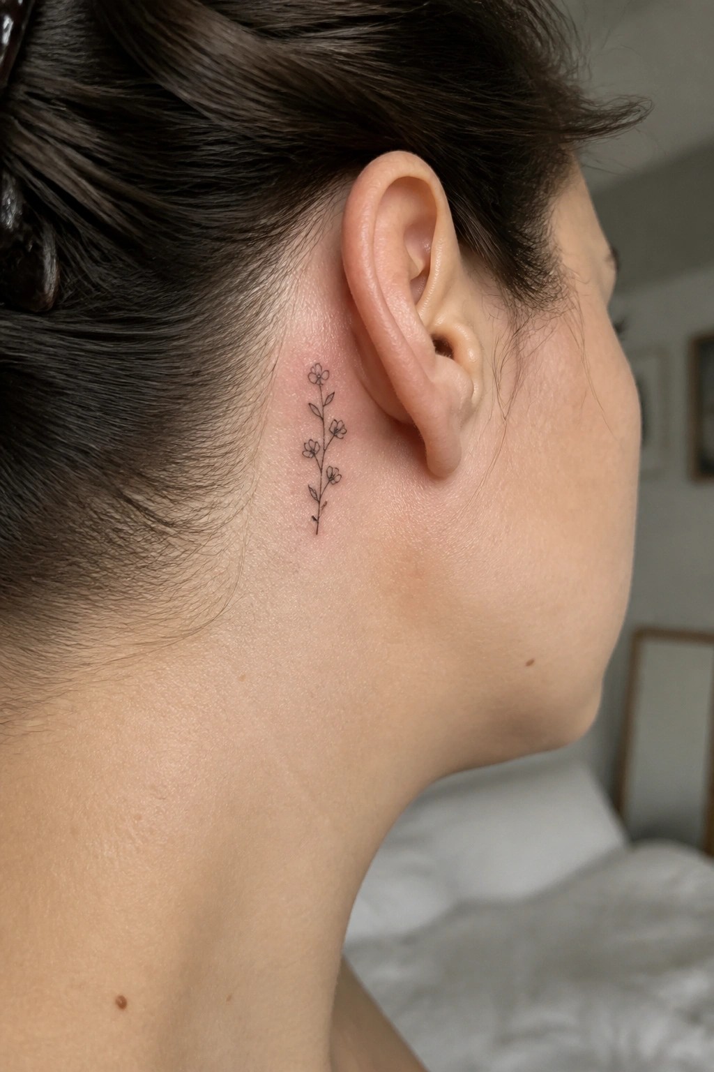 Small black floral vine tattoo behind ear on neck with dark hair pulled back.