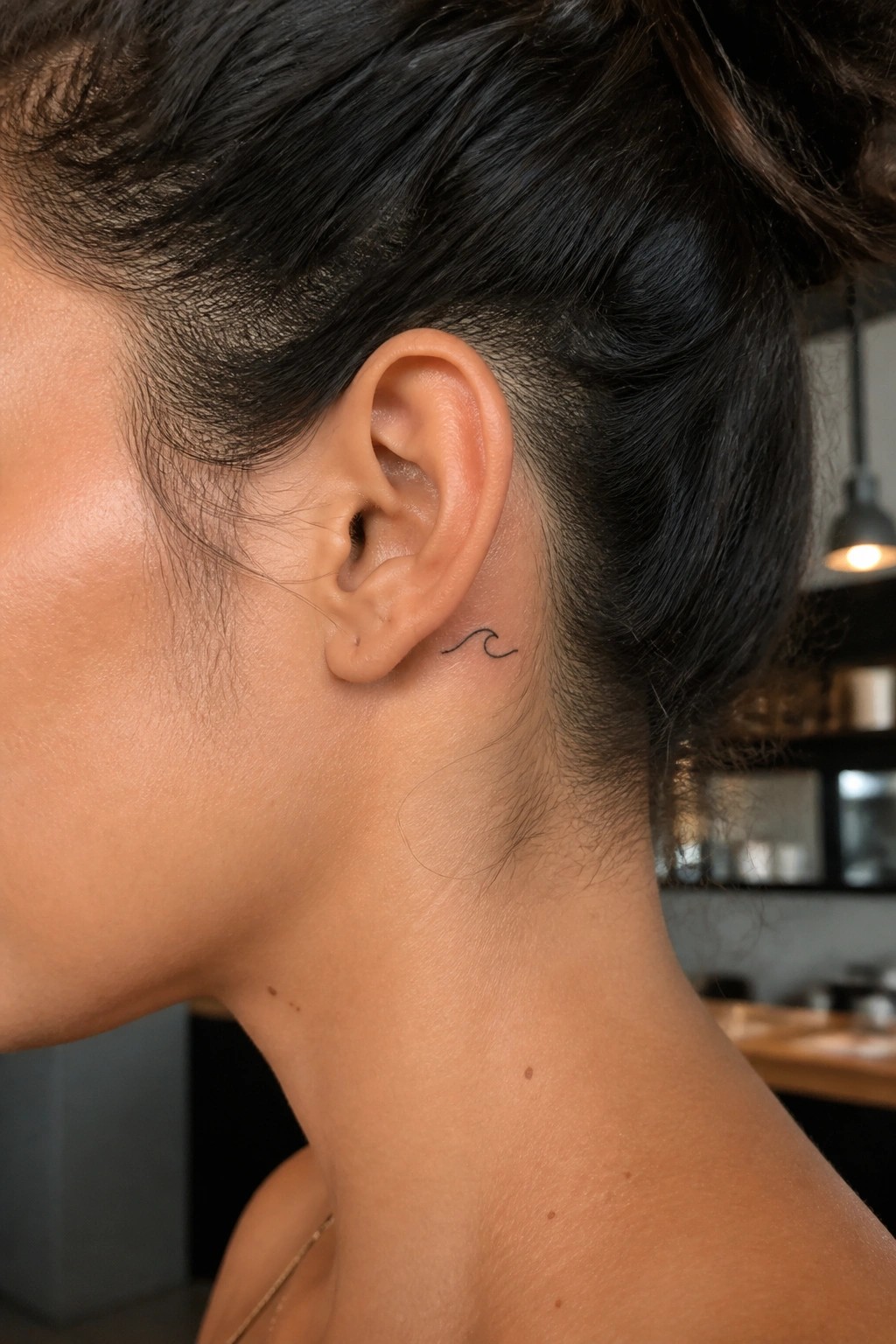 Close up of a small minimalist wave tattoo in black ink placed behind a woman's ear on the side of the neck.