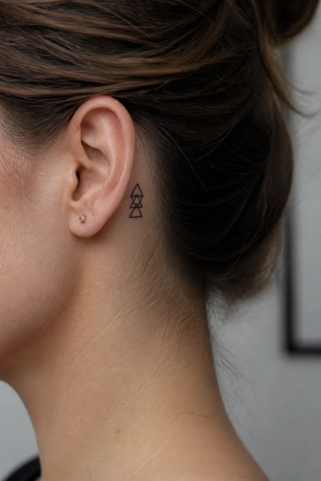 Woman's ear with gold stud earring and black geometric tattoo behind it.