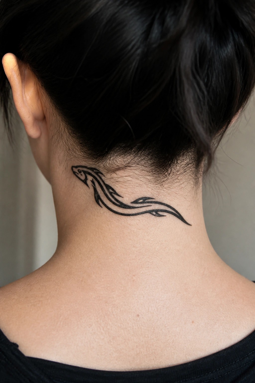 Black tribal fish tattoo spanning horizontally across the back of a neck, with dark hair pulled up to show the design.