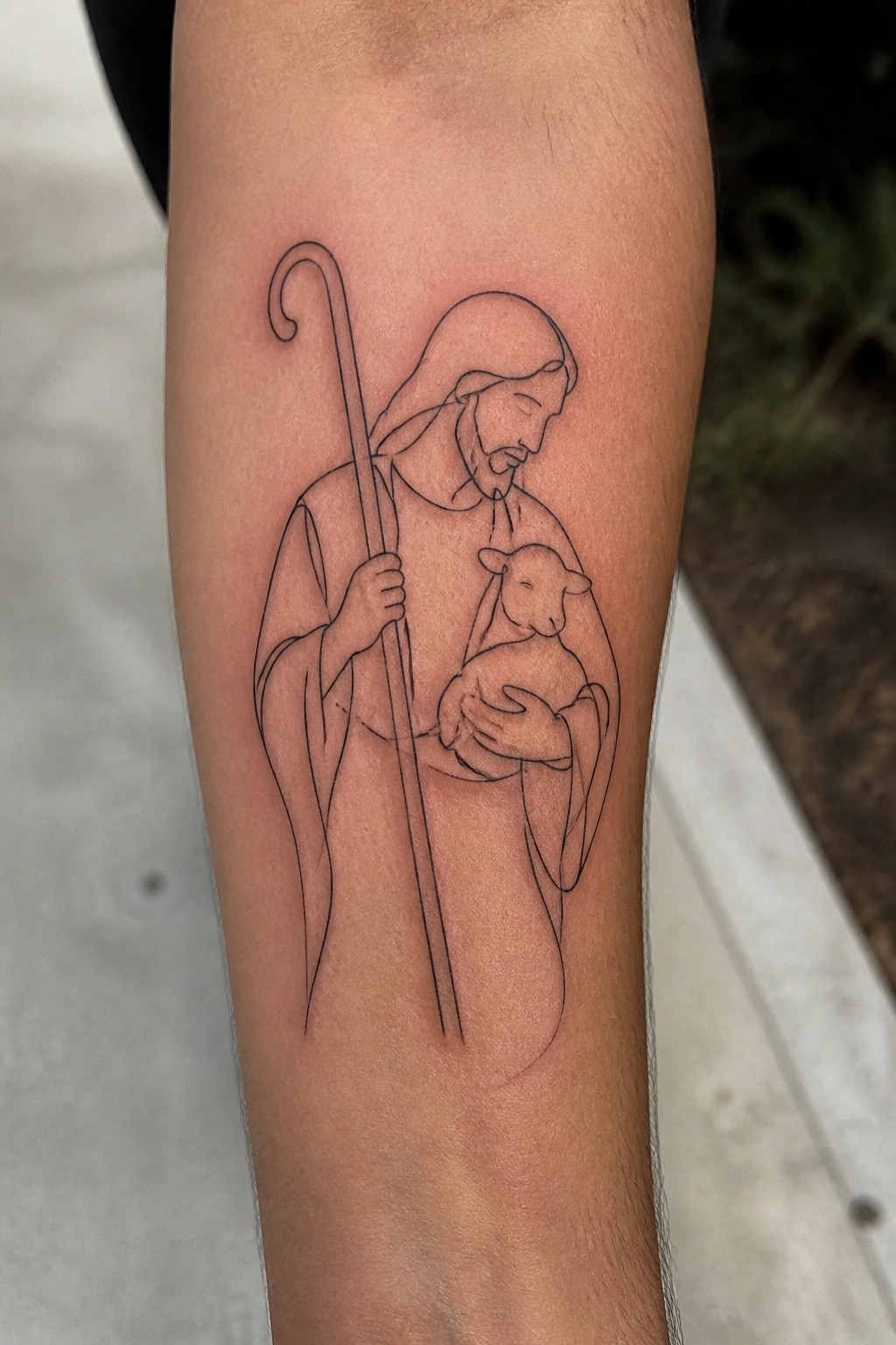 minimalist black line tattoo of jesus as shepherd holding a lamb on someone's forearm
