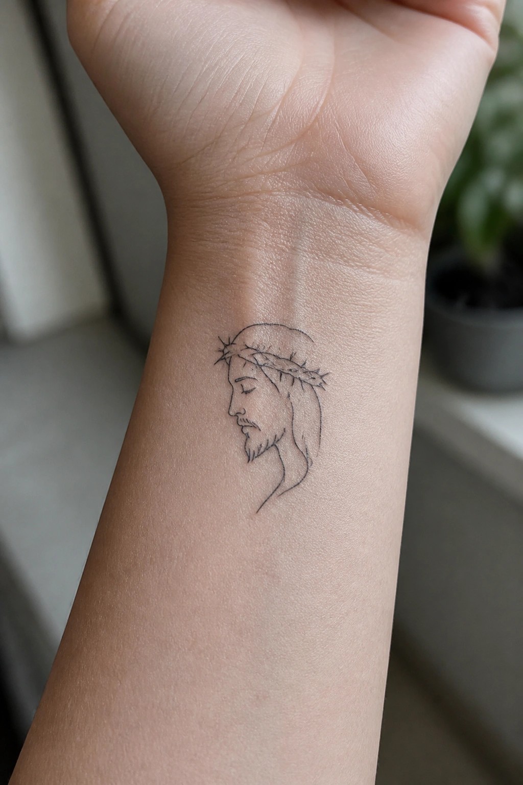 Small black outline tattoo of Jesus in profile with crown of thorns on the inner wrist