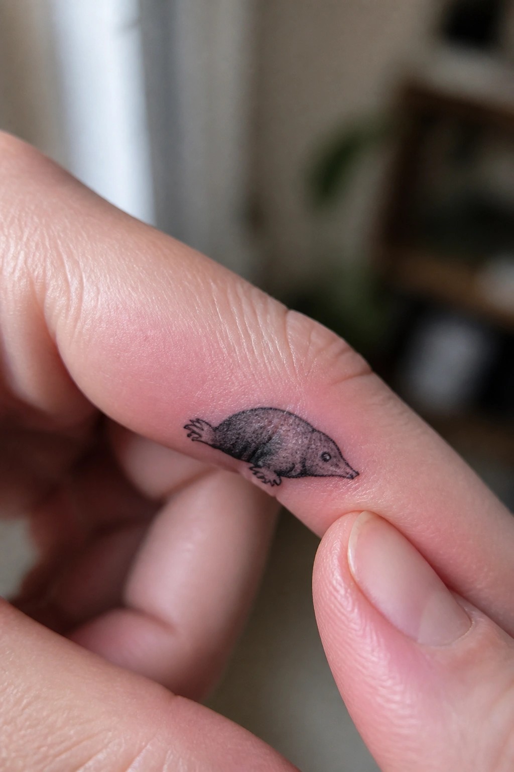 Small realistic black and gray mole tattoo placed on the side of a finger showing fine shading and simple details
