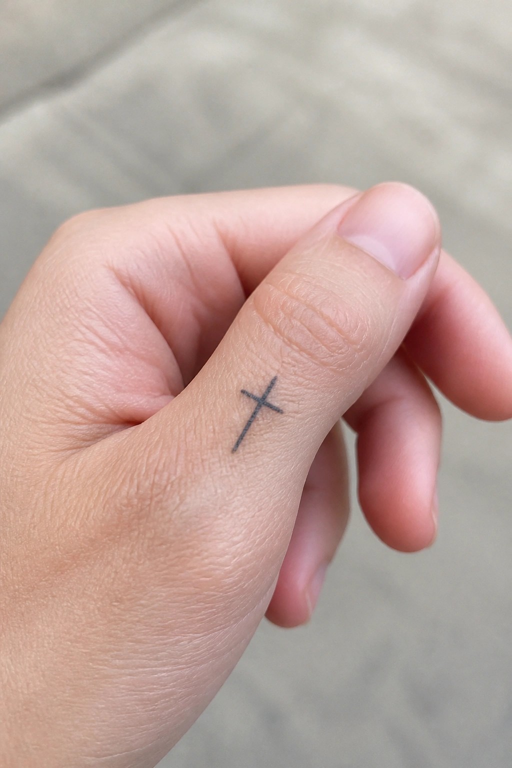 Small black cross tattoo on the side of a finger in simple line work