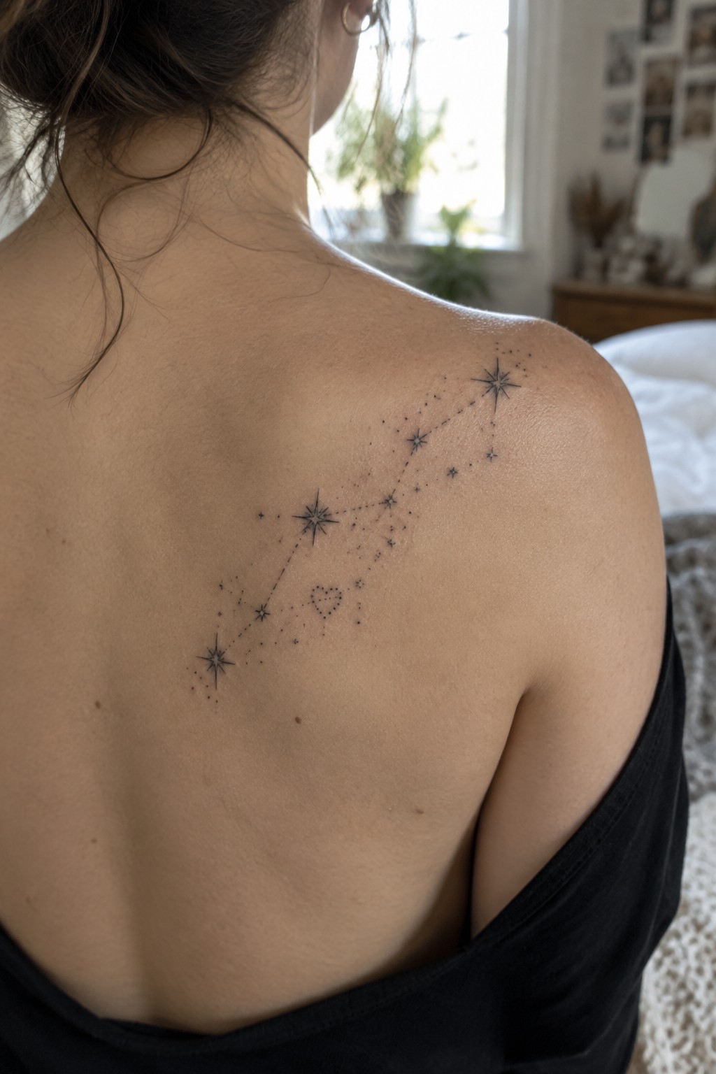 Woman's back with black constellation tattoo of stars and heart, black top lowered.