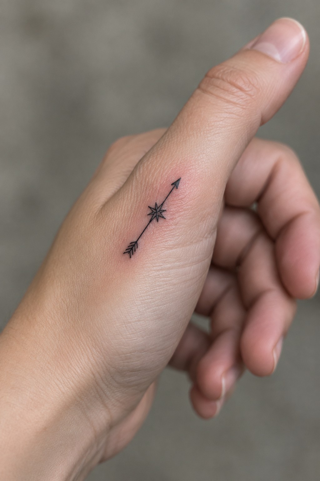 Close-up of a hand with a small black arrow and star tattoo on the finger.