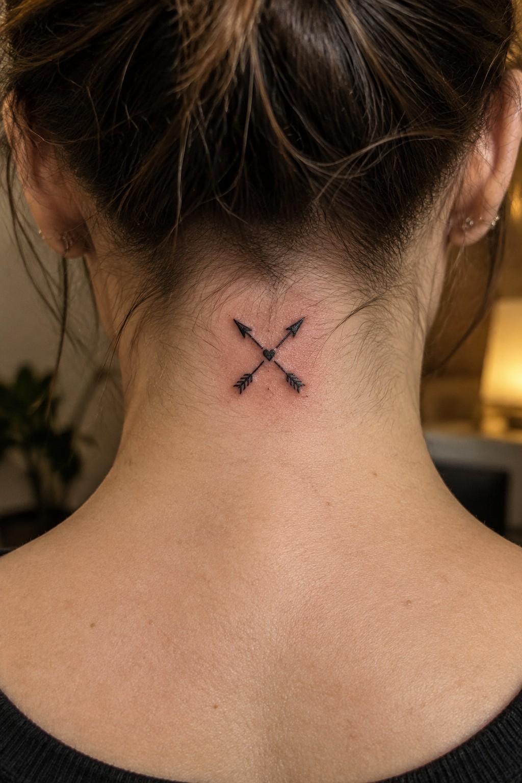 Crossed arrows and heart tattoo on the back of a neck with dark hair in a bun
