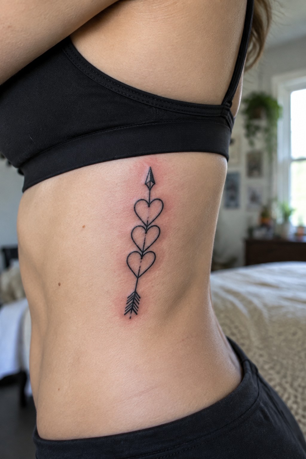 Fine line tattoo of an arrow with three hearts on the side of the ribs