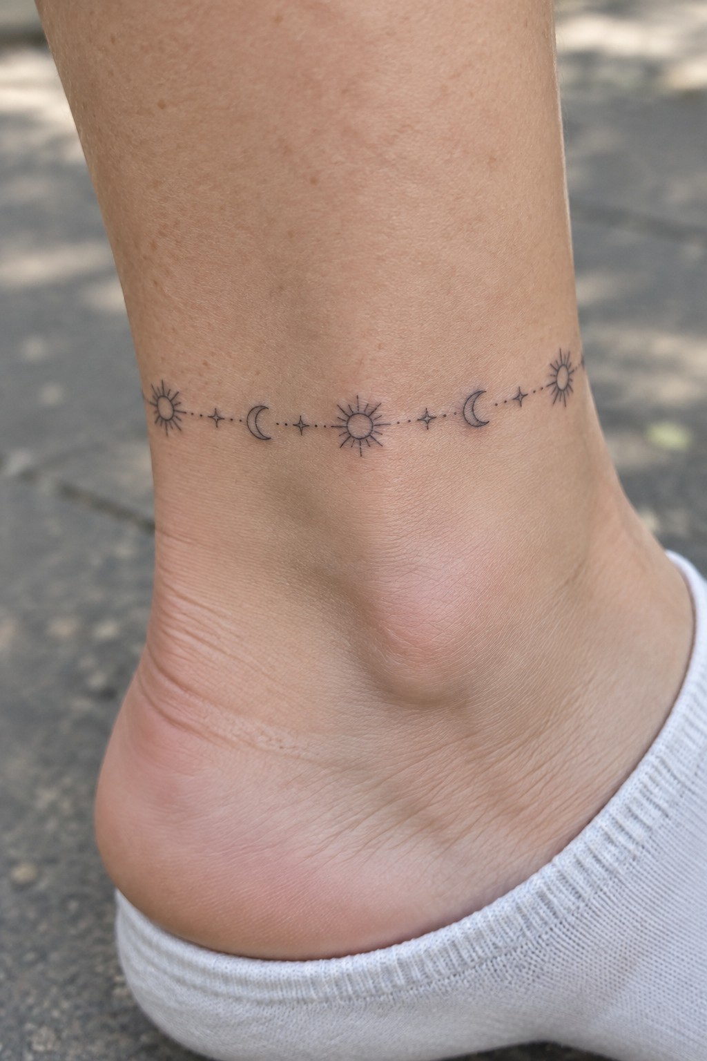 Ankle with celestial tattoo of suns, moons, stars, and dotted lines above white sock.