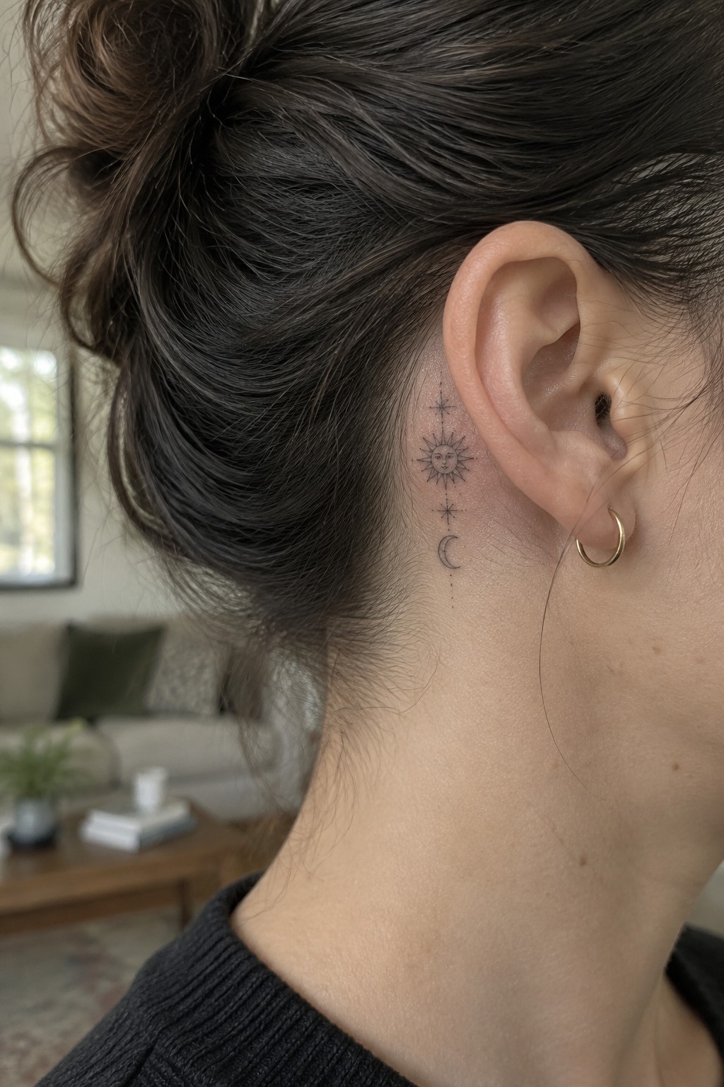 Dark bun hairstyle with celestial sun moon stars tattoo behind ear and gold hoop earring