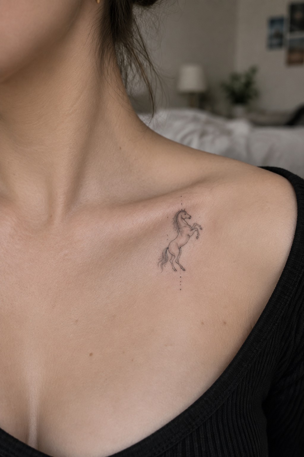 Woman's shoulder with delicate rearing horse tattoo above black top.