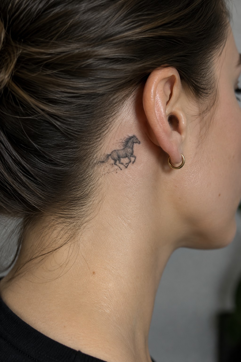 Woman's neck with running horse tattoo behind ear and gold hoop earring