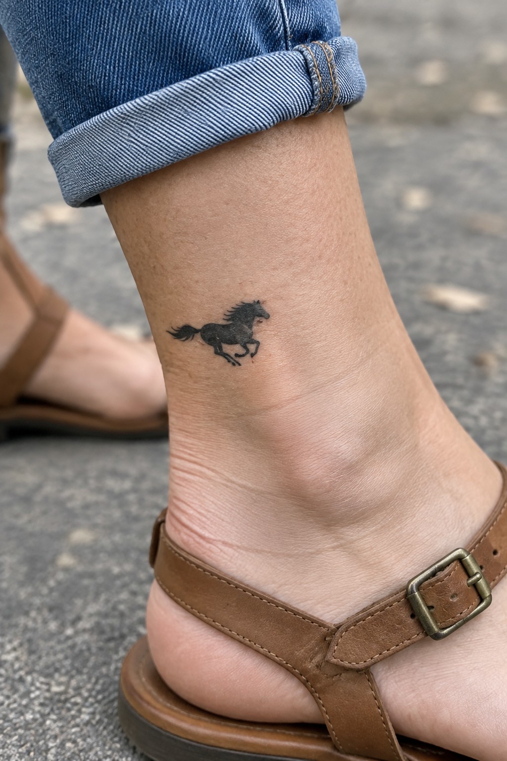 Black horse tattoo on ankle with rolled blue jeans and brown sandal