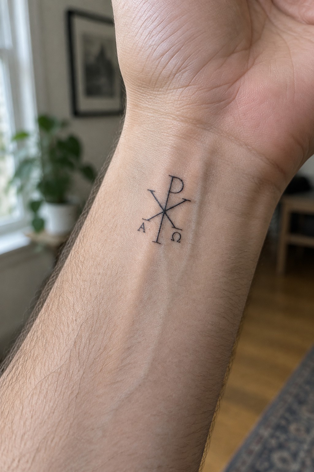Small chi rho tattoo with alpha and omega in black ink on the inner wrist