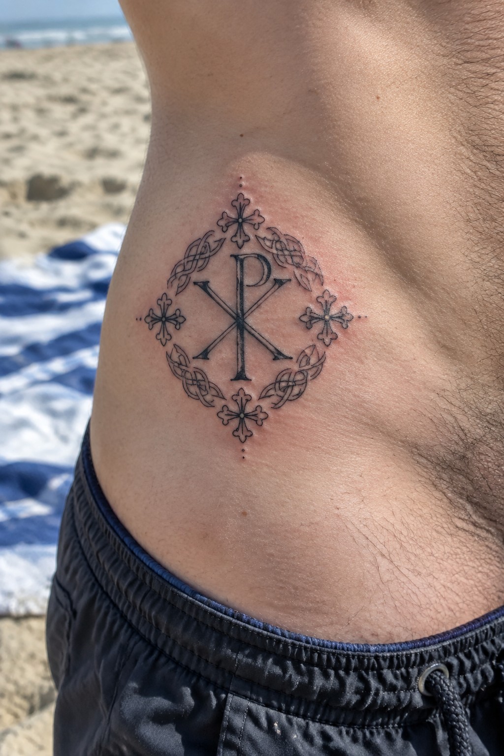 Fresh Chi-Rho tattoo with crosses and knots on man's chest at beach