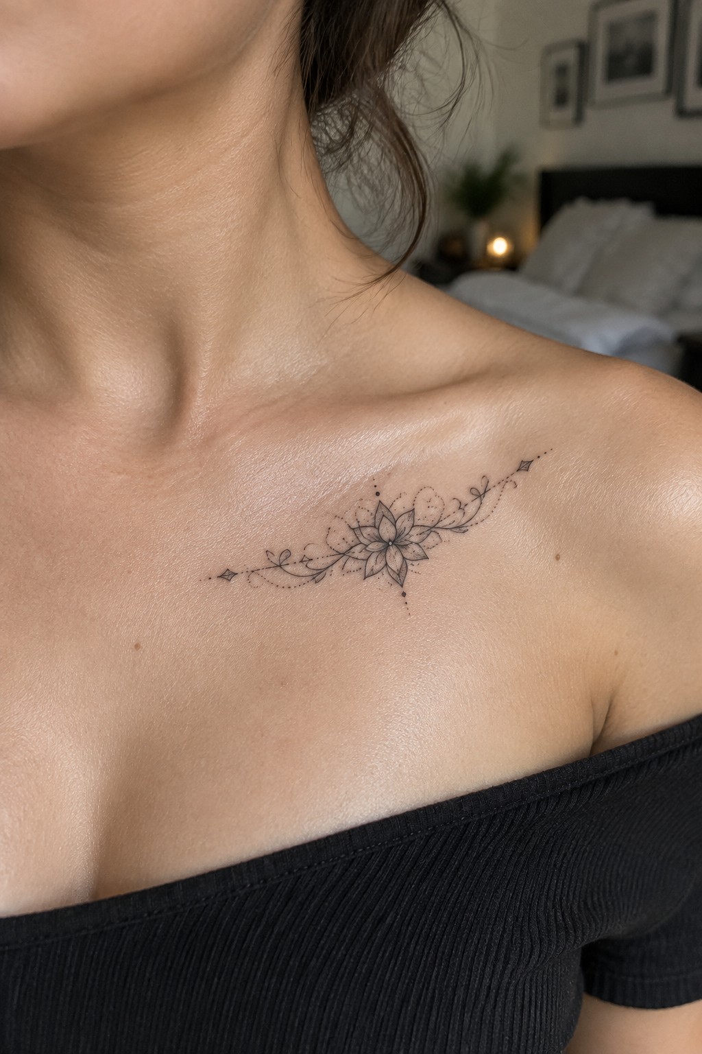 Small black dotwork mandala tattoo with a central flower and dotted vine extensions placed horizontally below the right collarbone on a woman's upper chest.