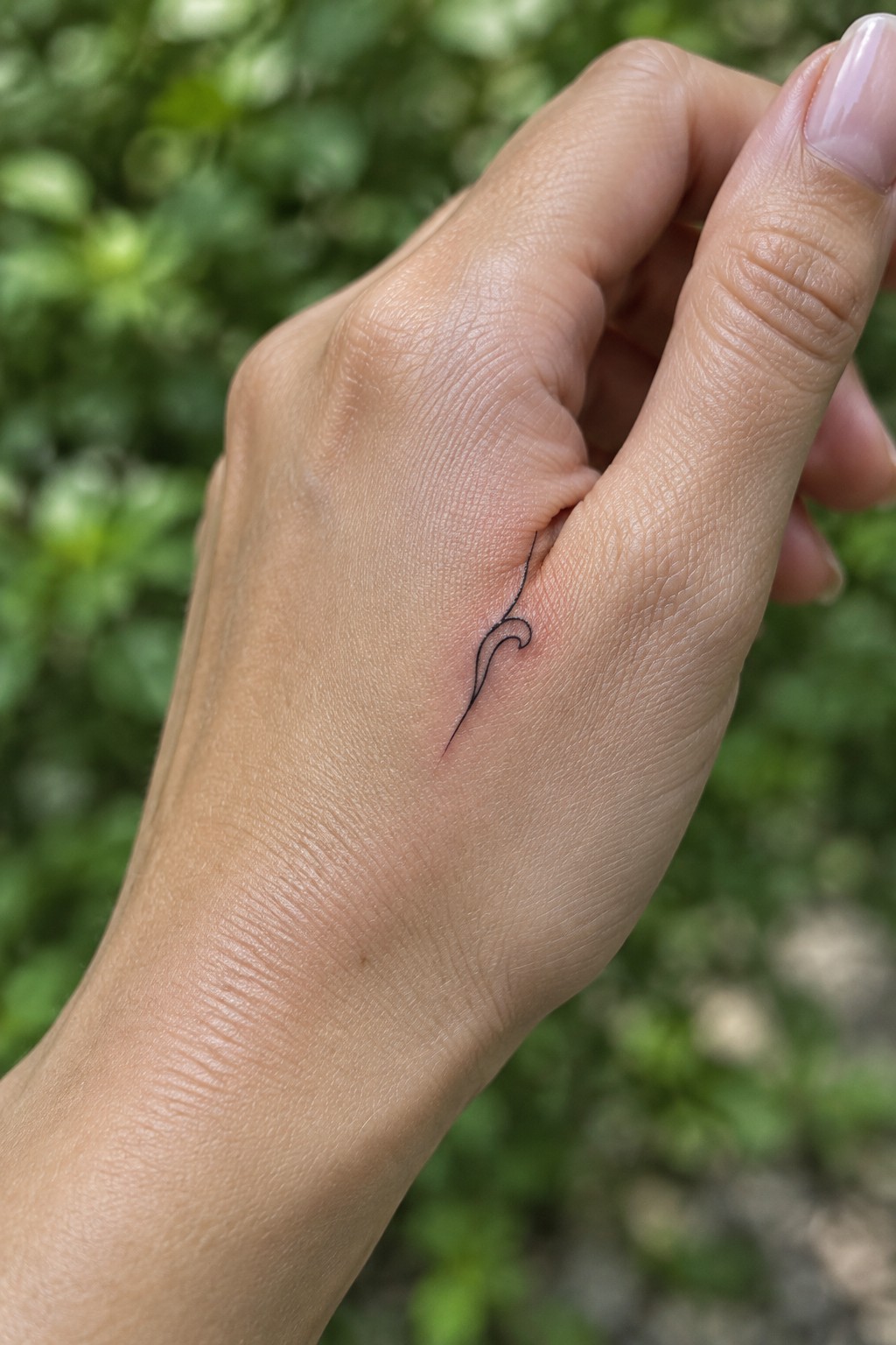 Hand with small black wavy abstract tattoo on side near fingers.