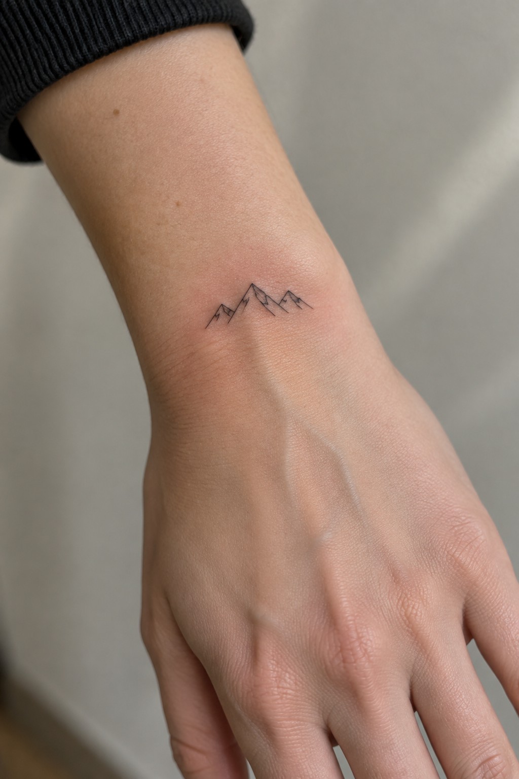 Small fine line mountain range tattoo on the inner wrist in black ink