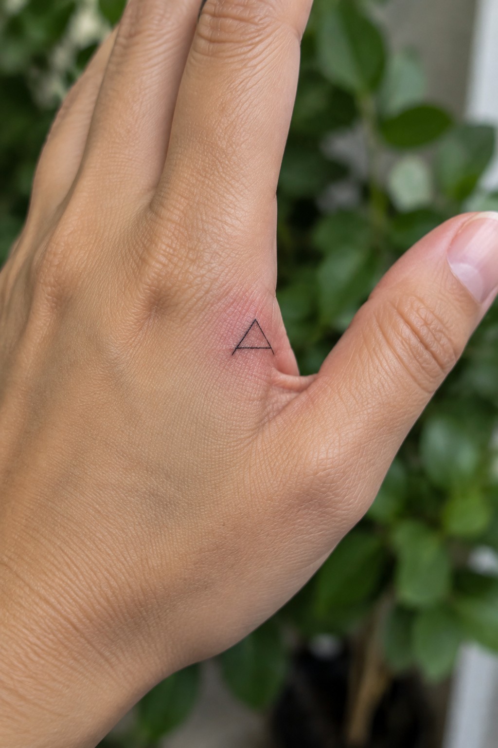 Close-up of light skin hand showing small black triangle tattoo on finger knuckle