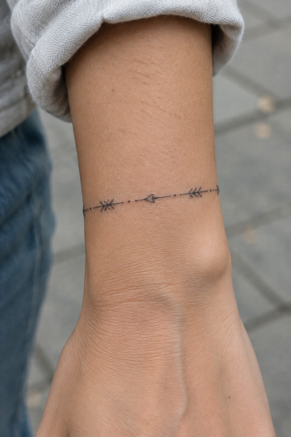 close up of a fine line wrist tattoo with small arrows and dots forming a horizontal band on light skin