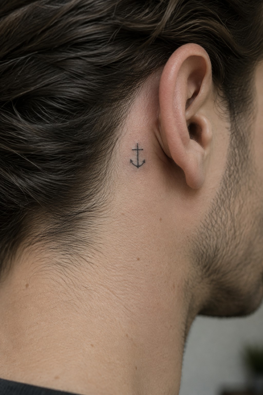 Small black anchor tattoo behind a man's ear on his neck