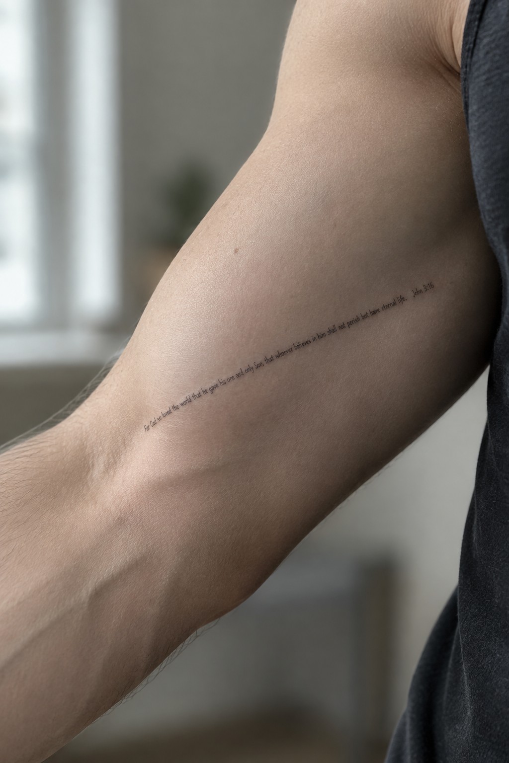 Person's upper arm with black John 3:16 Bible verse tattoo and dark shirt.